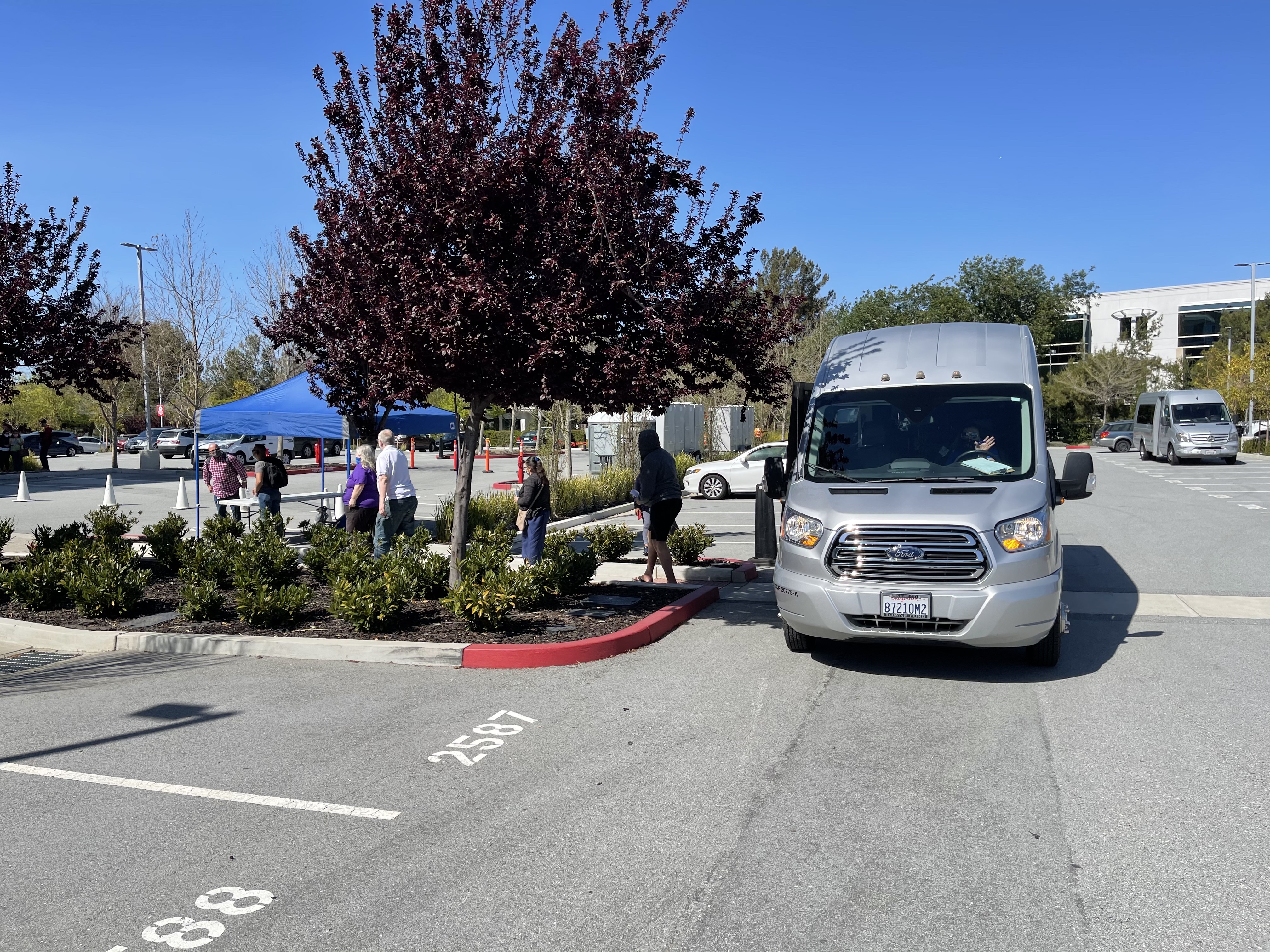 Shuttle in parking lot in front of a tent with a line of people